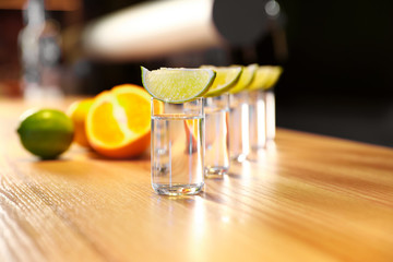 Vodka shots and lime slices on wooden bar counter