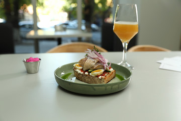 Tasty fish sandwich and glass of beer on light table