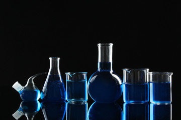 Laboratory glassware with blue liquids on black background