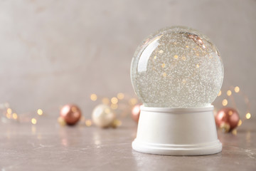 Snow globe and Christmas decorations on marble table against festive lights, space for text