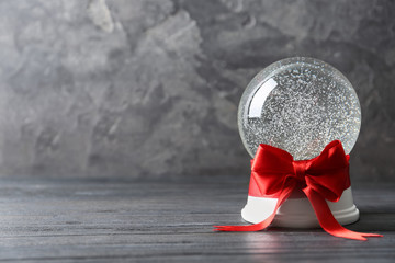 Beautiful Christmas snow globe with red bow on grey wooden table, space for text
