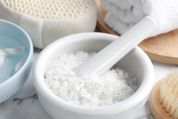 Mortar and pestle with white sea salt for spa scrubbing procedure on marble table