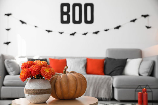 Modern room decorated for Halloween, focus on table with pumpkin and flowers. Festive interior