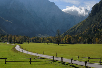 Early autumn in Logarska dolina (Logar valley) in Slovenia  beautiful landscape with green grass, road and wooden fence in the foreground, and with the mountain peaks and clouds in the background © Linda