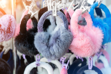 Lot of many multicolored bright fluffy warm winter fur earphones and gloves hanged on rack at store display for sale. Cute cold season clothes accessories