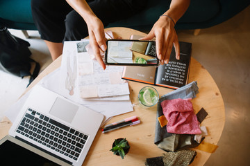 Close-up of fashion designer working on a new collection at desk taking smartphone picture
