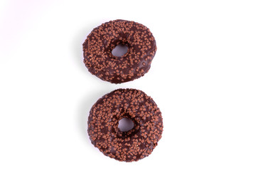 On a white background are two chocolate donuts, covered with icing and powder, one above, the other below. Highlighted in close-up.