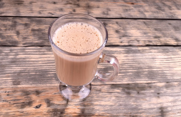 A cup of hot coffee with milk foam in a glass cup standing on wooden background