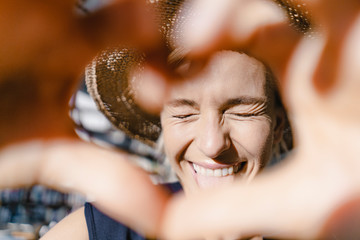 Woman with straw hat, looking into the sun, making heart shaped finger frame