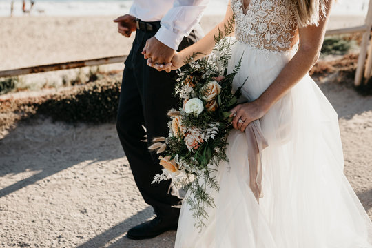 Close-up of bride and groom walking on path at the coast