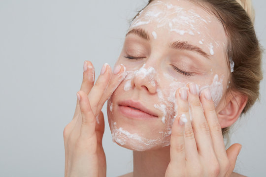 Portrait of blond young woman with eyes closed applying cream on her face