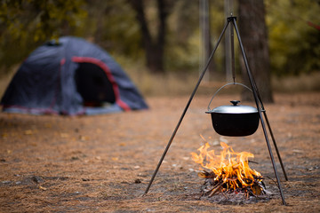 Hiking pot in bonfire with blue tent in autumn forest traveling