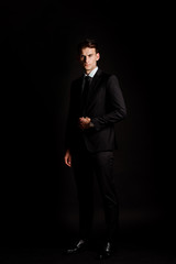 handsome businessman in suit standing isolated on black