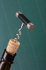 Corkscrew and wine bottle over green background