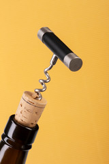 Corkscrew and wine bottle over yellow background