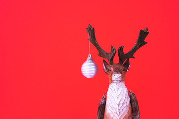 Funny Christmas wood reindeer with small festive ball on a red background. Minimalism holiday concept. New year toy