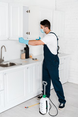 exterminator standing near kitchen cabinet and toxic equipment on floor