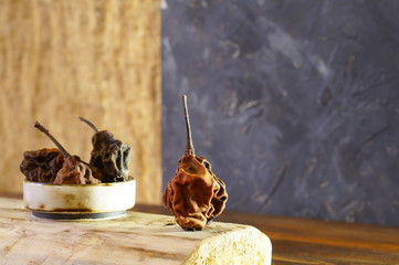 The composition consists of dried, wrinkled, dark pears in a ceramic saucepan on a light background and one brown pear, close-up on a dark background.