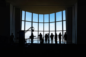 Silhouette of many friend taking photos at high floor of skyscraper neat huge panoramic windows with the view of the city.