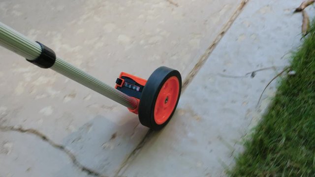 Measuring wheel tool calculating distance on damaged concrete patio. Outdoor surveying measurement tool with rolling odometer.