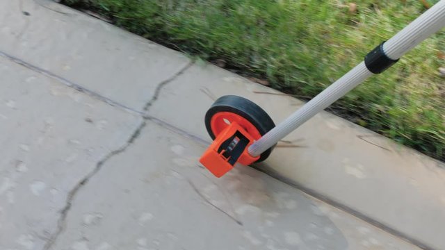 Measuring wheel tool calculating distance on damaged concrete patio. Outdoor surveying measurement tool with rolling odometer.