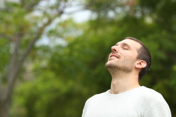 Happy man breathing deeply fresh air in a forest