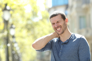 Fototapeta premium Stressed adult man suffering neck ache in the street