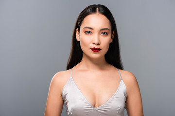 brunette attractive asian woman in satin dress with red lips isolated on grey