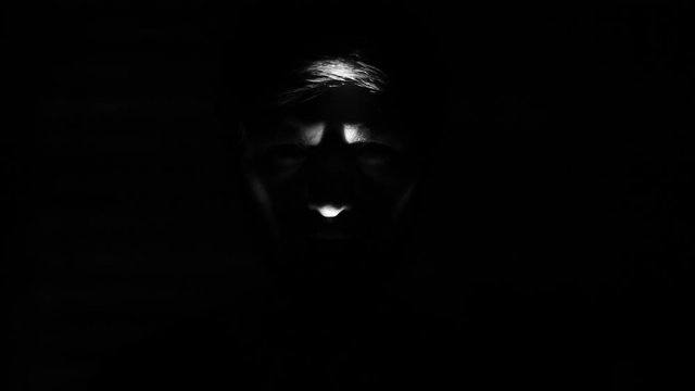 Dark portrait of creepy face selected with light. Black and white.