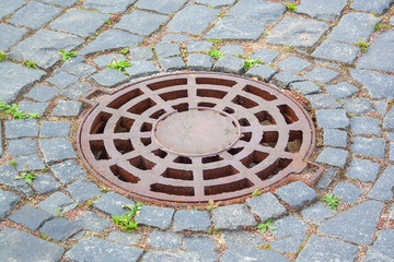 Manhole cover near paving stones. Rusty manhole cover on the walkside with paving stones