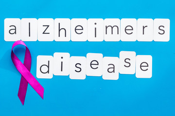 Alzheimers disease text near violet ribbon on blue background top view copy space