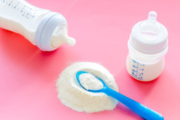 Baby food. Powder in spoon near baby bottle on pink background