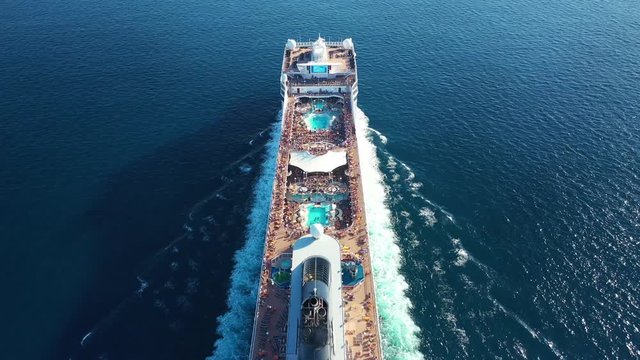 Aerial drone tracking video of huge cruise liner with pools and outdoor facilities cruising the Atlantic blue ocean