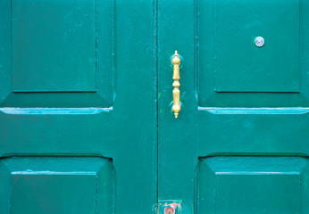 Old worn dark green door with a peeping hole and a door handle.