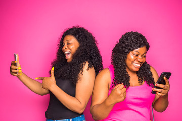 two pretty ladies feeling excited with they saw on their cellphone. ladies enjoys online communication, browse internet on modern smart phone, isolated over pink wall