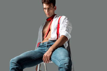 hot young man in white shirt sitting on chair on grey