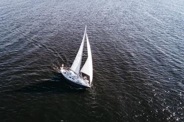 Aerial photography of yacht with white sails in dark blue open space. The good wind fills sails on a sunny summer day.