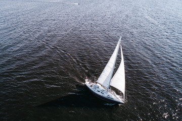 Aerial photography of yacht with white sails in dark blue open space. The good wind fills sails on...