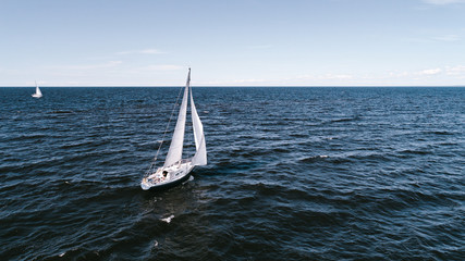 Aerial photography of yacht with white sails in dark blue open space. The good wind fills sails on a sunny summer day.