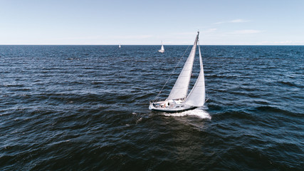 Aerial photography of yacht with white sails in dark blue open space. The good wind fills sails on a sunny summer day.