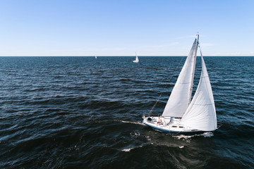 Aerial photography of yacht with white sails in dark blue open space. The good wind fills sails on a sunny summer day.