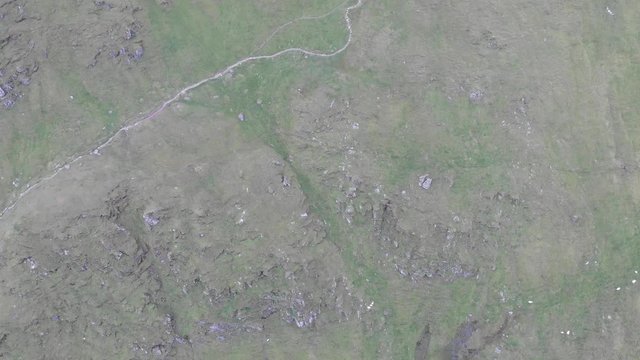 An aerial forward reveal footage of a grassy mountain rocky summit with small pond and mountain range in the background under a cloudy sky
