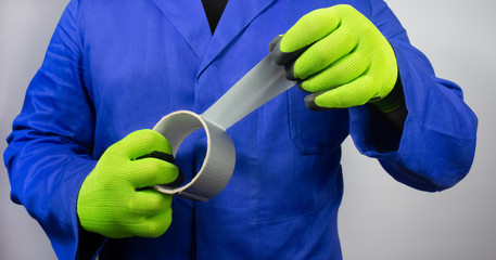 Worker in blue outfit and gloves holding duct tape.