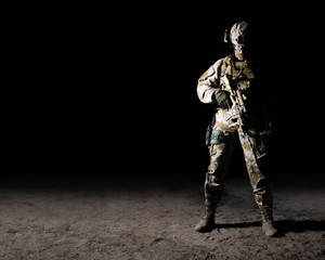 Fully equipped soldier standing with rifle on dark background.