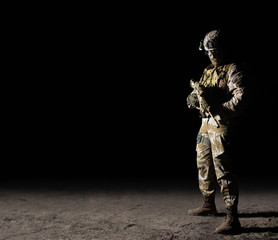 Fully equipped soldier standing with rifle on dark background.