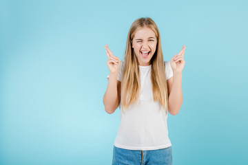 happy young girl with fingers crossed hoping and praying for luck isolated over blue