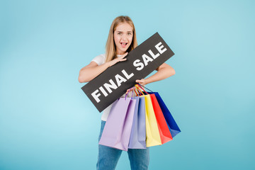 excited girl with final sale sign and colorful shopping bags isolated over blue