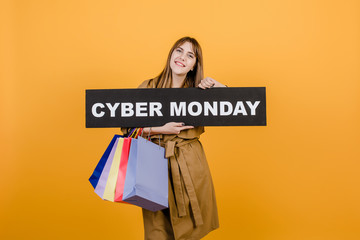 smiling happy woman with cyber monday sign and colorful shopping bags isolated over yellow