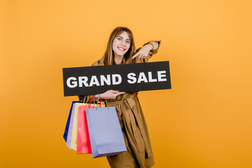 young beautiful woman with grand sale  sign and colorful shopping bags isolated over yellow