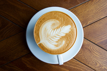 A large mug of fragrant cappuccino, on a saucer and a wooden table.